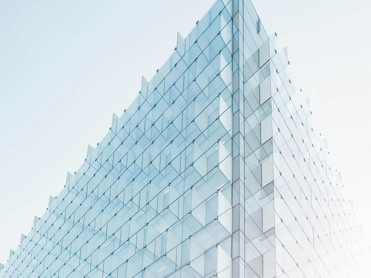 Glass curtain-wall facade of a modern tower rising into a pale sky