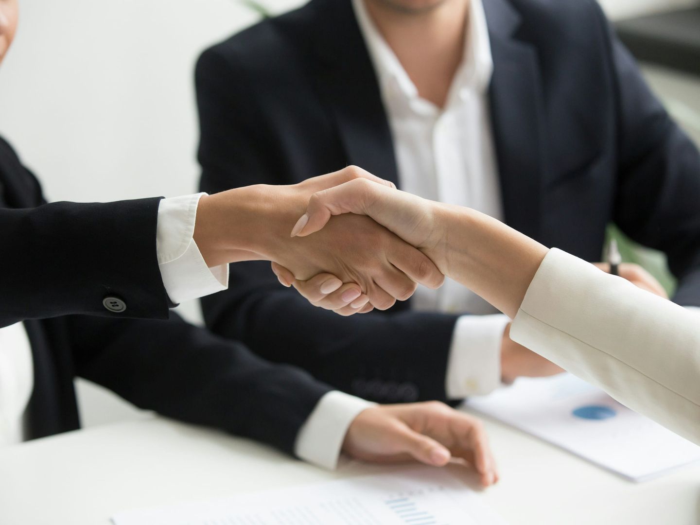 Two people shaking hands across a table after signing an agreement